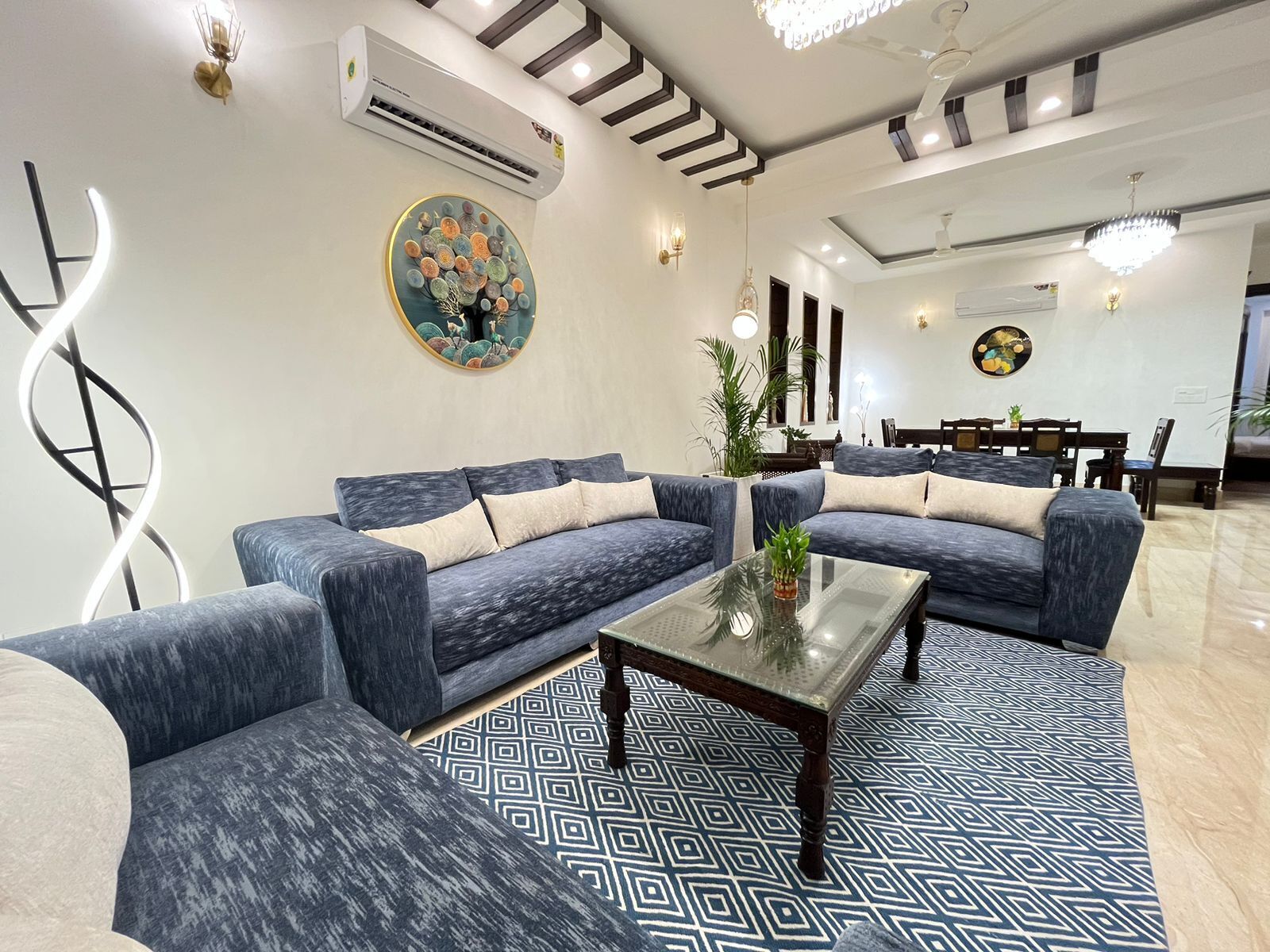 A modern living room with a blue sofa set, a glass coffee table, and a patterned rug.