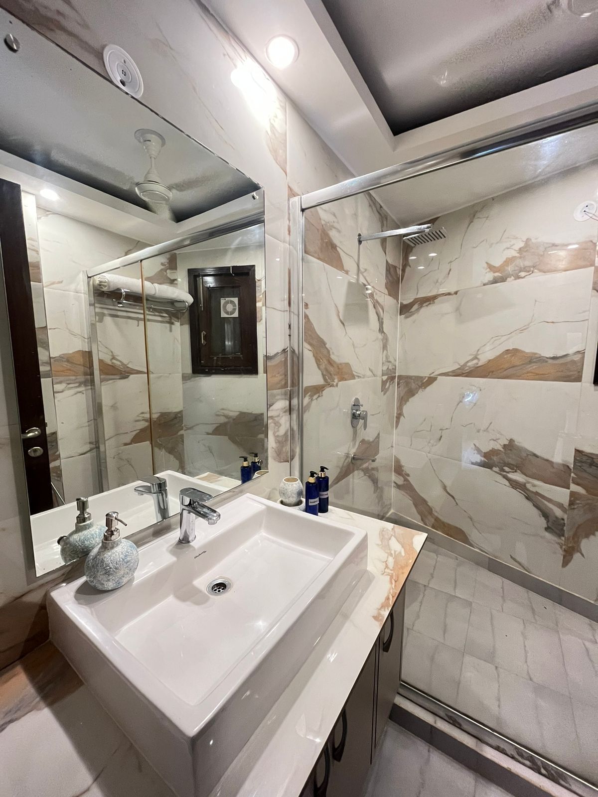 A modern bathroom with a large mirror, a white sink, and a glass-enclosed shower.