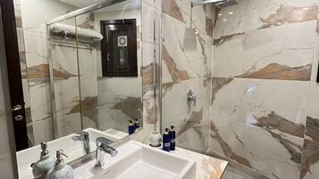 A modern bathroom with a large mirror, a white sink, and a glass-enclosed shower.