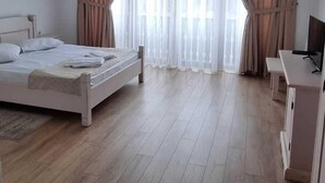 Une chambre spacieuse avec un grand lit, un bureau et une fenêtre avec des rideaux.