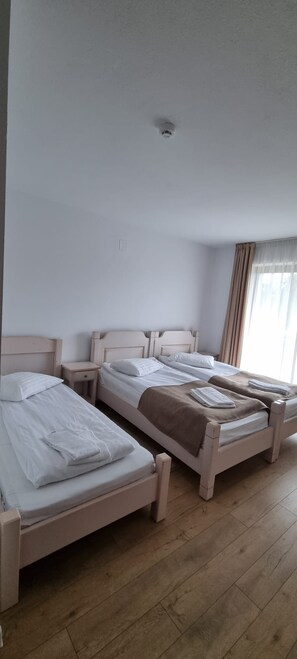 A hotel room with two single beds, a small bedside table, a ceiling light, and a window with curtains. - Complex turistic Panicel (Rasnov)