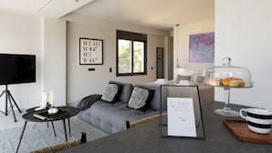 A modern living room with a grey sofa, black and white cushions, a flat-screen TV, a small coffee table, and a framed sign on the wall. - Athens Riviera Suites (Saronikos)