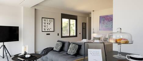 A modern living room with a grey sofa, black and white cushions, a flat-screen TV, a small coffee table, and a framed sign on the wall.