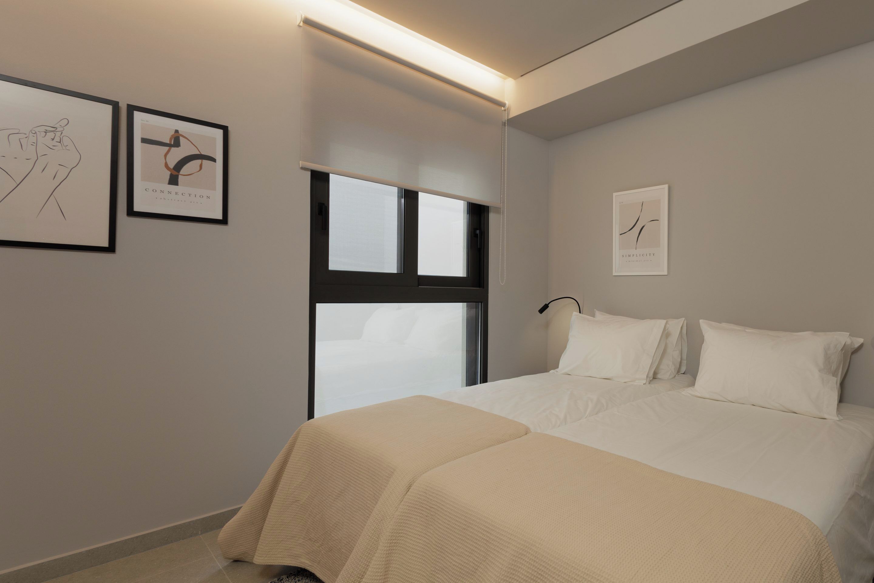 A bedroom with a bed, a window, and two framed artworks on the wall.