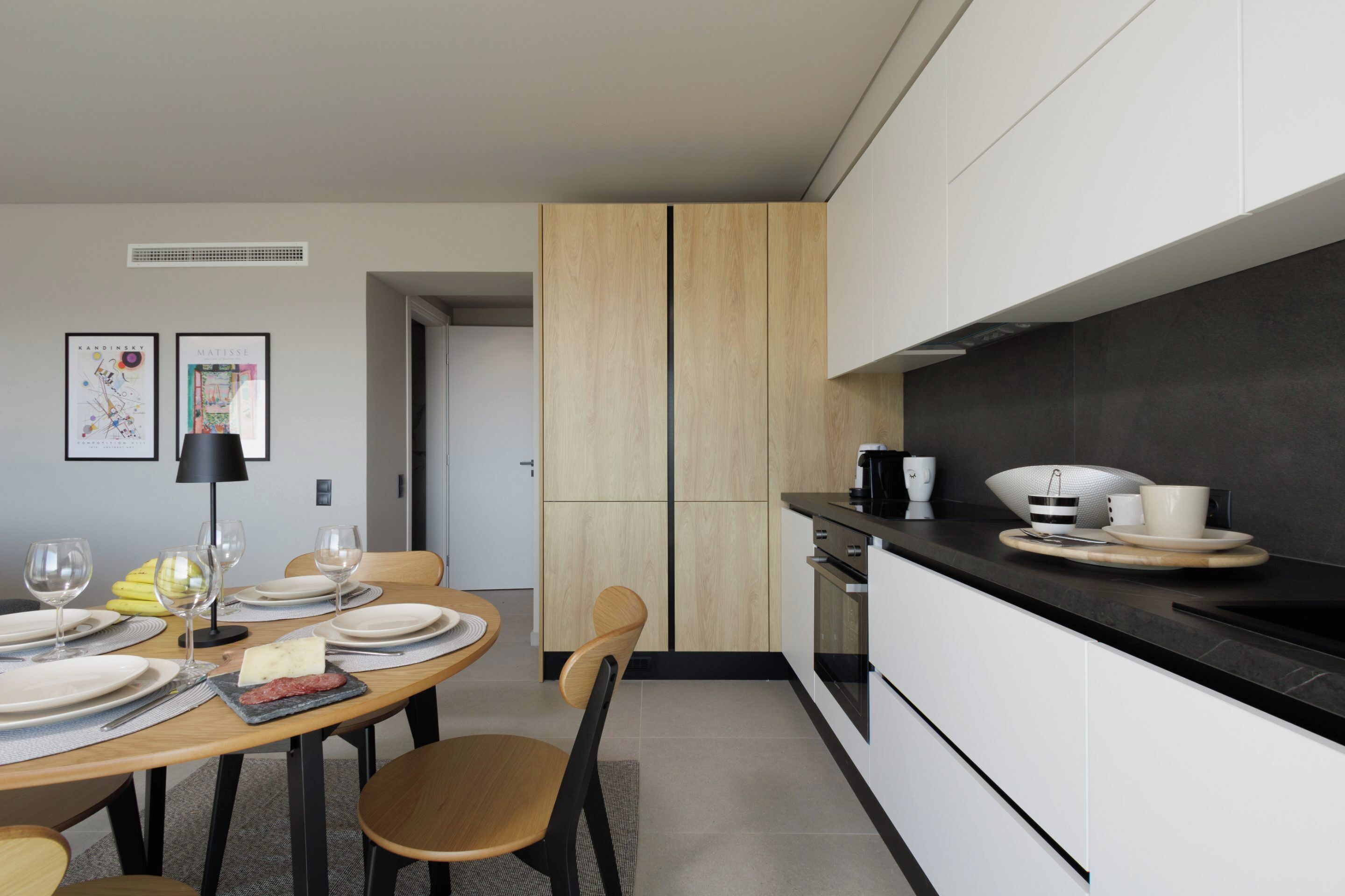A modern kitchen with a dining area. It includes a table set for two, a coffee maker, and a microwave.