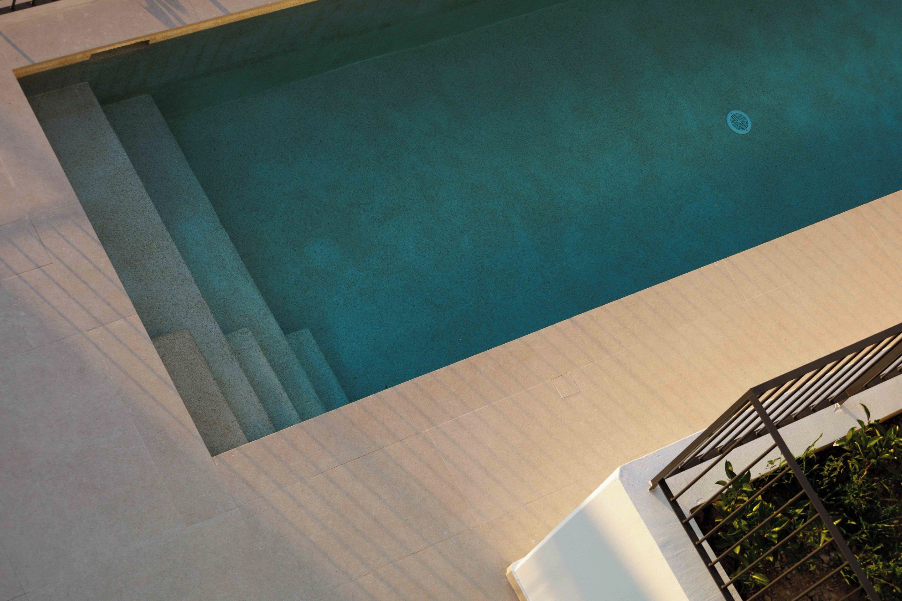 Una piscina con solárium empedrado y barandilla metálica.