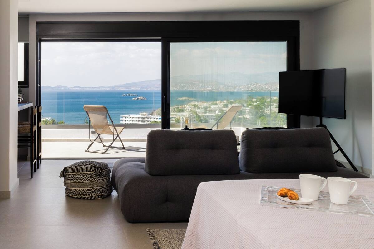 A modern bedroom with a large window, a sofa, a TV, and a breakfast tray.