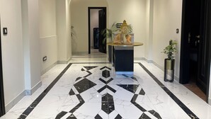 Un couloir doté d’un sol en marbre, d’une statue sur un piédestal et d’une porte noire sur le côté droit.