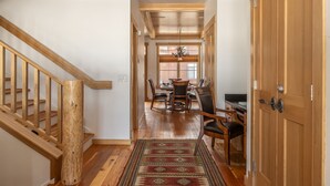 A wooden staircase leading to a dining area with a patterned rug and a chandelier. - Cross-Country Ski Out the Back Door (Big Sky)