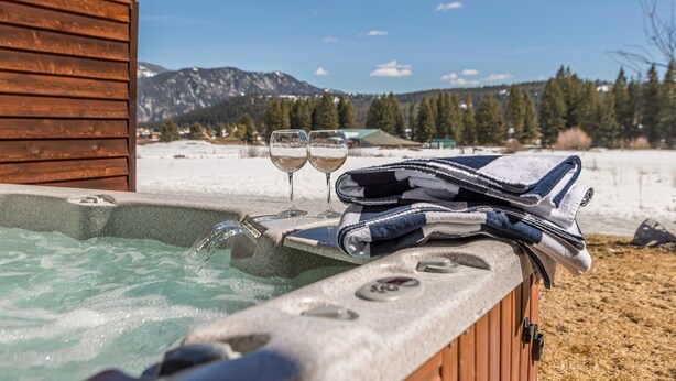 A hot tub with two glasses of white wine, a towel, and a wooden cabin in the background. - Cross-Country Ski Out the Back Door (Big Sky)