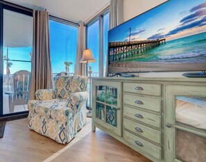 Ein Zimmer mit großem Fenster, einer Couch, einer Kommode und einem Gemälde eines Piers.