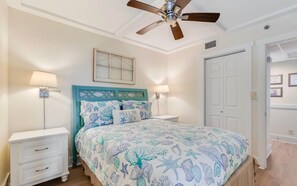 Ein Schlafzimmer mit einem Bett, zwei Nachttischen, einem Deckenventilator, einer Tür und einer Wandleuchte.