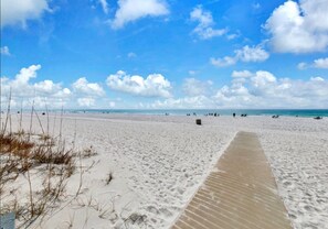 Una playa arenosa con un paseo marítimo de madera que lleva al agua.