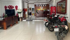 A hotel lobby with a reception desk, a television, a coffee machine, and a motorcycle parked by the wall.