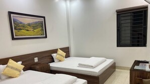 A hotel room with two beds, a desk, a chair, a window with blinds, and a framed painting on the wall.