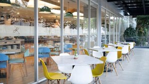 A modern dining area with glass walls, yellow and white chairs, and tables. - Laska Hotel Subang (Subang)