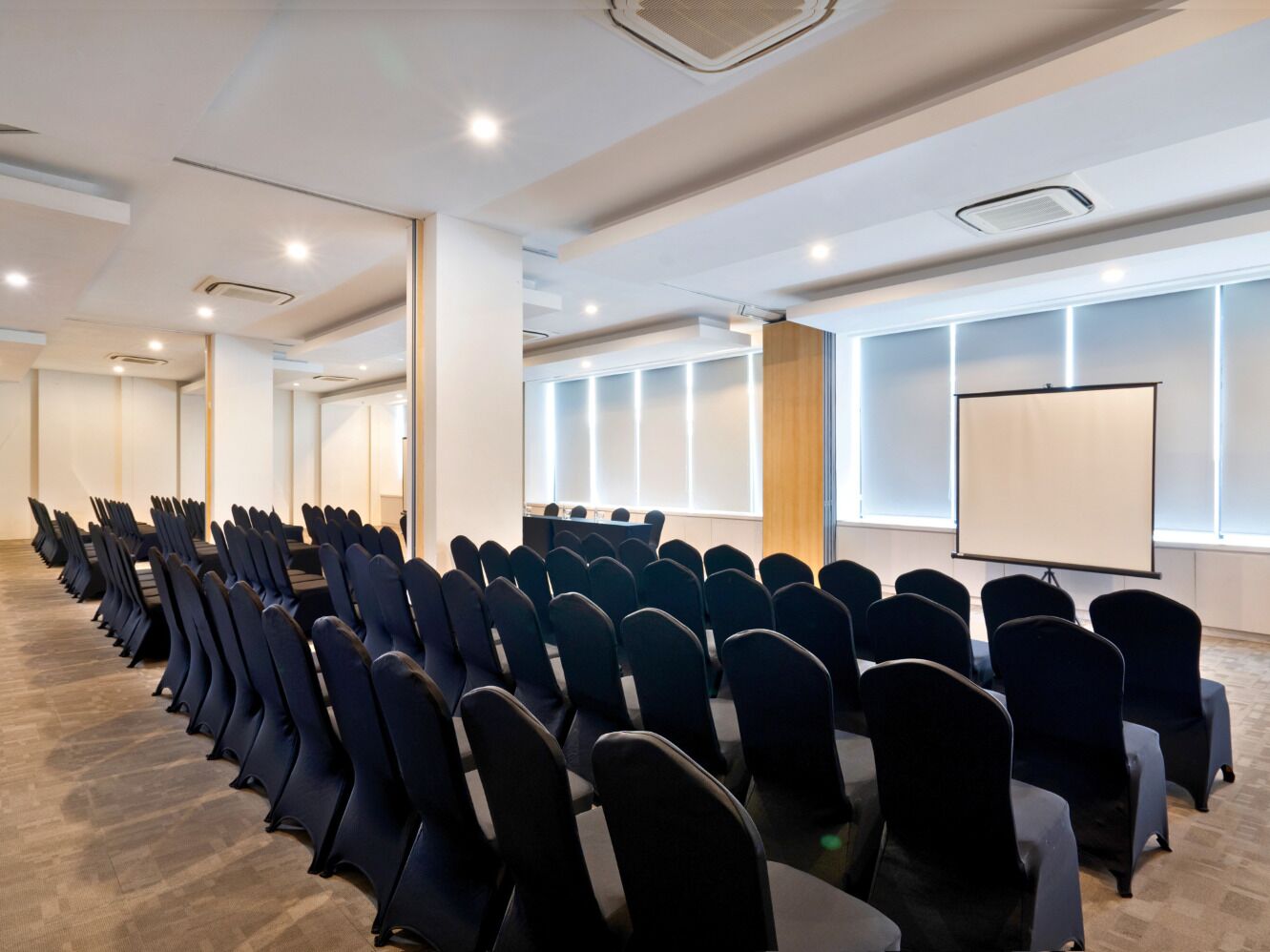 A conference room with rows of chairs, a projector screen, and a presentation screen.