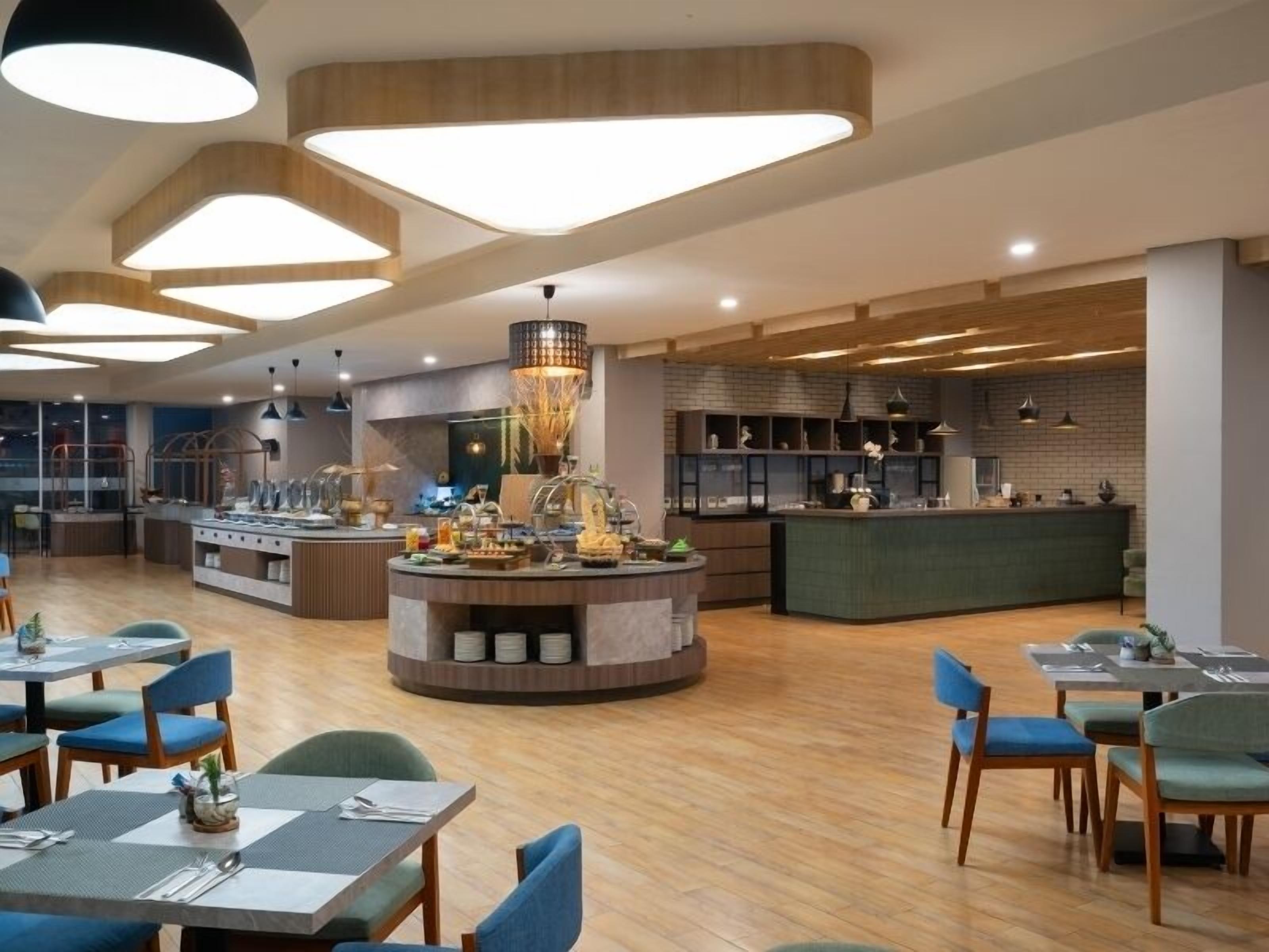 Un restaurant moderne doté d’un îlot central, de plusieurs tables et d’un espace cuisine situé à l’arrière-plan.