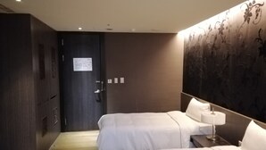 Habitación de hotel con dos camas, una puerta de madera oscura, un papel tapiz floral y suelo de madera.