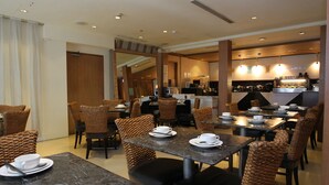 Un comedor de hotel con mesas y sillas de mimbre, una cocina al fondo y una puerta de madera.