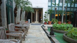 Un patio con suelo de piedra, mobiliario de madera y plantas en macetas.