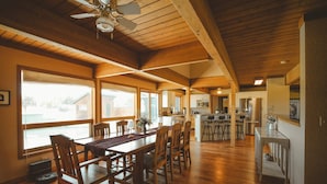 Cocina amplia con armarios de madera, una isla central con taburetes y vistas al exterior a través de ventanas grandes.