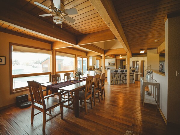 Cocina amplia con armarios de madera, una isla central con taburetes y vistas al exterior a través de ventanas grandes.