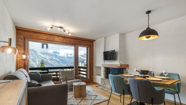 Un salon moderne doté d’une grande fenêtre, d’un plafond en bois et d’un coin repas avec une cheminée.