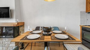 Un coin repas avec une table en bois dressée pour quatre personnes, un luminaire suspendu moderne et une cheminée en pierre.