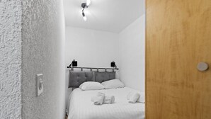Une chambre à coucher avec un lit, des murs blancs, une porte en bois et un luminaire au plafond.