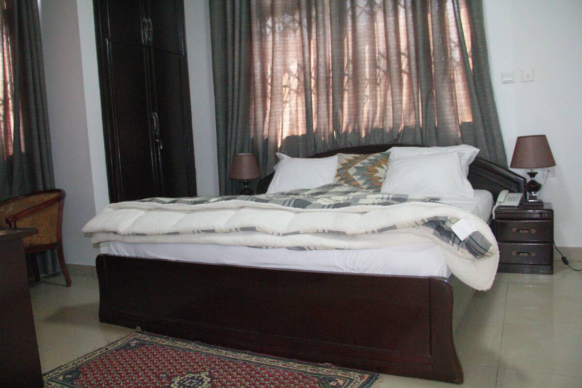 Une chambre avec un grand lit, une table de chevet avec une lampe, une chaise en bois et un tapis à motifs.