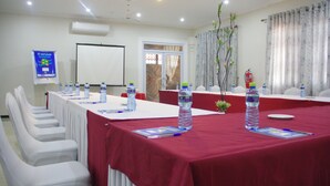 Una sala conferenze con un lungo tavolo, sedie bianche, bottiglie d'acqua e uno schermo per proiezioni.