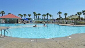 A swimming pool with clear blue water, surrounded by palm trees and a fenced area.