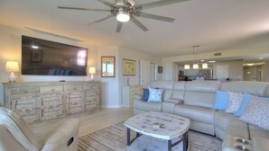 A spacious living room with a large sofa, a coffee table, and a ceiling fan.