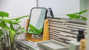 Un baño con un espejo sobre un pedestal de madera, una planta en maceta y una pared de azulejos a rayas.