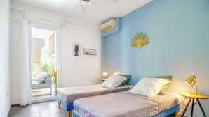 Un dormitorio con dos camas, un ventilador de techo, un equipo de aire acondicionado y una mesita de noche con lámpara.