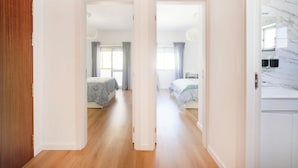 A hallway leading to two bedrooms with wooden flooring, a bathroom with a marble countertop, and a view of the outside through a window. - Lovely 2 bed apartment in quiet Lisbon South Bay - Close to the best beaches! (Baixa da Banheira)