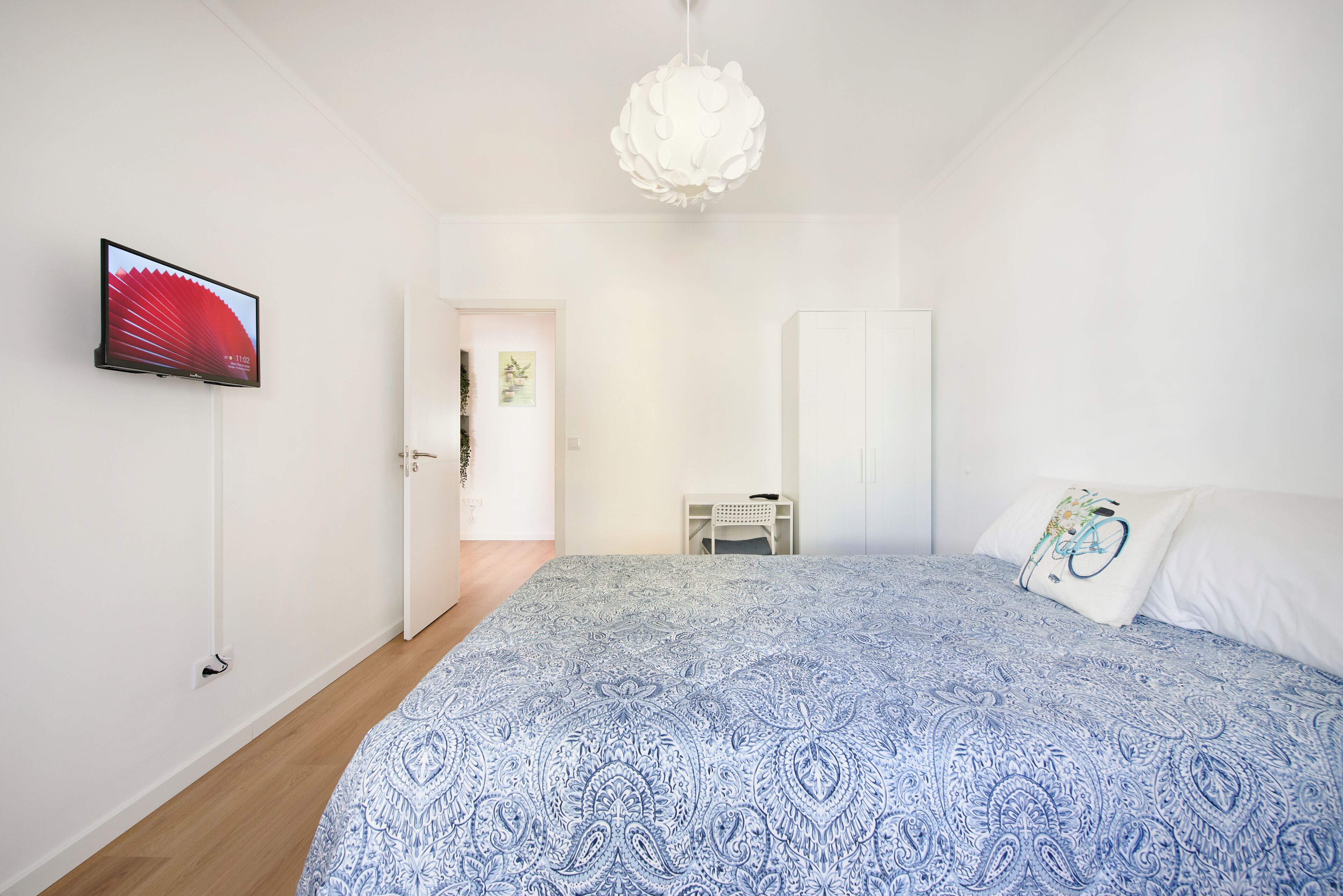 Ein Schlafzimmer mit einem Bett, einem Fernseher, einem weißen Kleiderschrank und einer Tür zu einem anderen Raum.