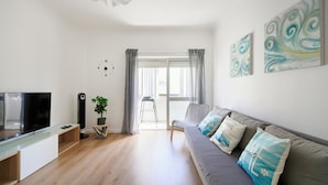 A modern living room with a flat-screen TV, a sofa with decorative pillows, a side table with a plant, and abstract wall art. - Lovely 2 bed apartment in quiet Lisbon South Bay - Close to the best beaches! (Baixa da Banheira)