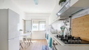 A modern kitchen with white cabinets, a wooden countertop, and a built-in stove. There is a window with blinds, a sink, and a bar stool. - Lovely 2 bed apartment in quiet Lisbon South Bay - Close to the best beaches! (Baixa da Banheira)