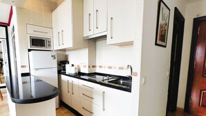 A compact kitchen with white cabinets, a black countertop, a built-in microwave, a coffee maker, and a sink. - Mediterraneo 702. Super Studio with Amazing Sea Views (Marbella)