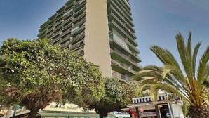 A high-rise building with multiple balconies, surrounded by trees and palm plants. - Mediterraneo 702. Super Studio with Amazing Sea Views (Marbella)
