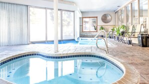 Une piscine intérieure bordée de carreaux, une pièce lumineuse avec de grandes fenêtres et un coin salon avec des fauteuils et des plantes en pot.