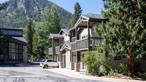 Un immeuble à plusieurs étages doté de balcons, entouré d’arbres et avec une montagne en arrière-plan.