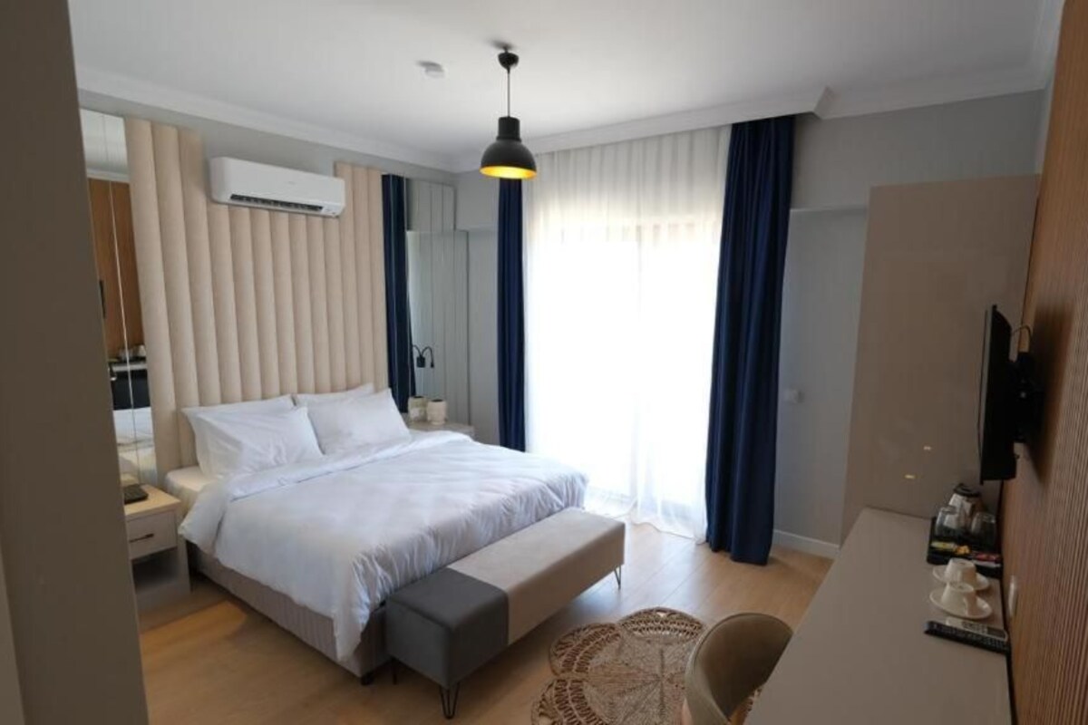 A modern hotel room with a large bed, bedside tables, a flat-screen TV, and a large window with curtains.