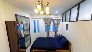 A bedroom with a bed, a wardrobe, a chandelier, and a window with curtains. - Roscotel Bay Stays 2BHK Near White Town (Puducherry)