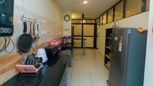 A kitchen with a black countertop, a refrigerator, and a wall-mounted rack holding kitchen utensils. - Roscotel Bay Stays 2BHK Near White Town (Puducherry)