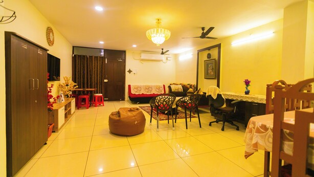 A well-lit living room with a chandelier, a dining area with a table and chairs, and a sofa. - Roscotel Bay Stays 2BHK Near White Town (Puducherry)