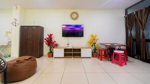 A living room with a flat-screen TV, a wooden cabinet, a bean bag, a small table with two pink stools, and potted plants. - Roscotel Bay Stays 2BHK Near White Town (Puducherry)