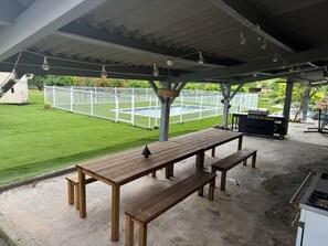 A covered patio area with a wooden table and benches, a barbecue grill, and a fenced backyard with a pool. - Huge estate with swimming pool, cinema, reception hall, boules pitch and more (Nérac)